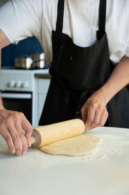 Eller hamuru pişirirken beyaz masa üzerinde merdaneyle