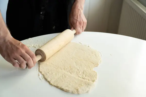 Eller hamuru pişirirken beyaz masa üzerinde merdaneyle