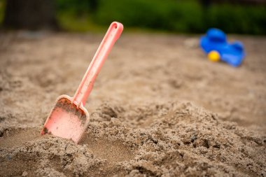 Küçük bir oyuncak kürek kum havuzundaki kuma saplanıyor.