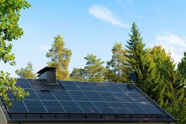 Güneş panelleri mavi gökyüzü ve ağaçlara karşı ev çatısı.