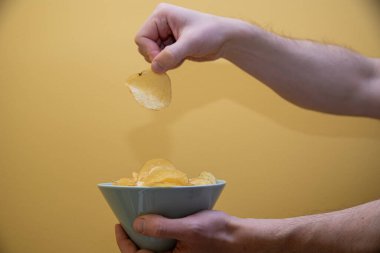Bir kaseden patates cipsi çıkarıyorum. sarı arkaplan.