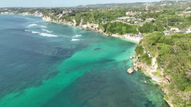 Güzel bir tropikal ada sahil şeridinin çarpıcı hava manzarası. Yemyeşil kayalıklar. Beyaz kum turkuazı okyanusu. Kumsaldaki güneş pansiyonları. Padang Padang Plajı Endonezya Bali. 4K dji Maviç 3 video. 