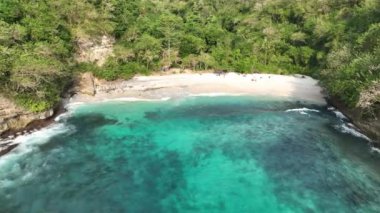 Küçük bir adası olan güzel bir tropikal sahil kuşbakışı manzarası. Beyaz kum turkuazı okyanusu. Kumsaldaki güneş pansiyonları. Pandan Sahili Endonezya Bali. 4K dji Maviç 3 video. 