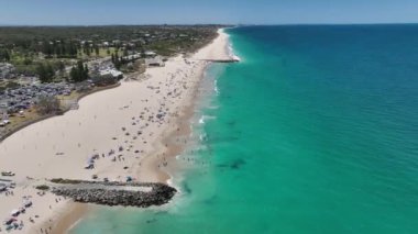 City Beach Perth Avustralya 'nın destansı hava manzarası. Yazın güneşlenen ve denizde yüzen bir sürü insan var. Batı Avustralya kıyı şeridi, insanlar tatilde. Hava aracı görüntüsü 4K. DJI Mavic 3