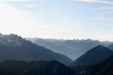 Şafak vakti katmanlı sıradağların nefes kesici manzarası. Siluetli tepeleri ayıran puslu vadiler, derinlik ve gizem hissi yaratıyor, uzak dağlar sisli mavi bir ufuk çizgisi içinde kayboluyor..