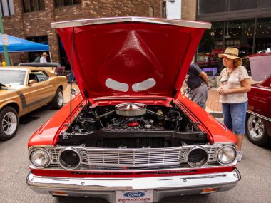 Bir araba fuarının hareketli atmosferine dalın. Canlı kırmızı bir araba, biraz altın ile, sahnenin ortasında yer alır. Kaputu açıkken, araba motorunu ve iç bileşenlerini gözler önüne seriyor ve performans yeteneğini ima ediyor..