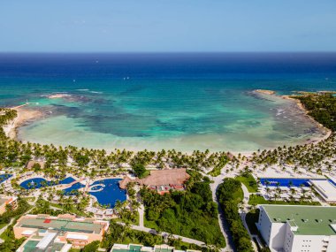 Görüntü, tropikal bir cennetin nefes kesici bir görüntüsü. Gök mavisi okyanusların yuva yaptığı bir tatil yeri. Tatil köyü el değmemiş bir plajla kaplanarak lüks ve doğanın mükemmel bir karışımını oluşturuyor. Çimenli ağaçlarla kaplı asfalt bir yol manzaraya ekleniyor.