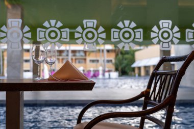 Zarif bir havuz başı masası. Bir bardak şarap, gümüş çatal bıçak takımı ve karmaşık bir şekilde tasarlanmış bir binanın yansıması..