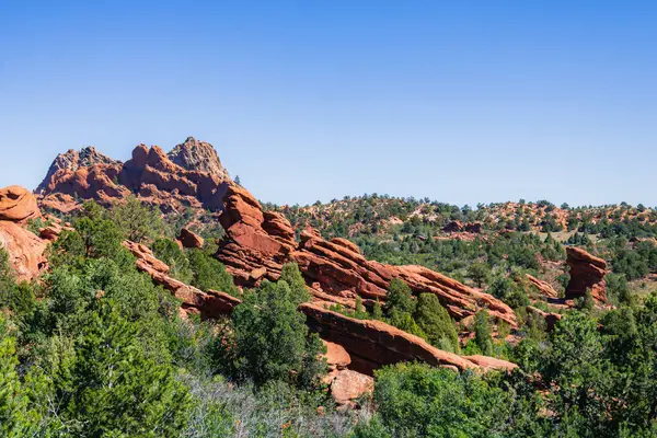 xperience the contrast of fiery red rocks against verdant foliage in this stunning landscape.