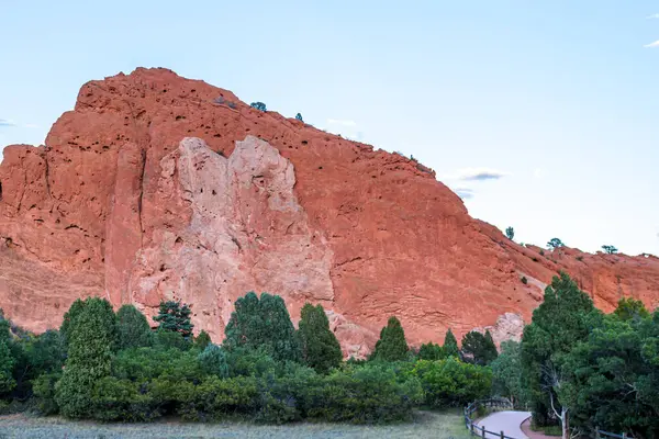 Stock image Last light of day illuminates a red rock cliff above a forest path.