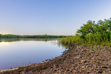 Sabahın erken saatlerinde Atoka Oklahoma Park 'ı kayalık bir kıyı şeridi ve yemyeşil bitki örtüsüyle gölün durgunluğunu yakalıyor. Huzurlu atmosfer yansıma ve doğa takdiri anları için mükemmeldir..