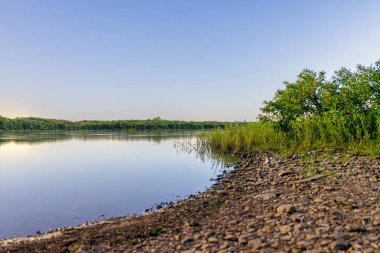 Sabahın erken saatlerinde Atoka Oklahoma Park 'ı kayalık bir kıyı şeridi ve yemyeşil bitki örtüsüyle gölün durgunluğunu yakalıyor. Huzurlu atmosfer yansıma ve doğa takdiri anları için mükemmeldir..