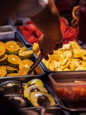 Bir el, Tayland 'da ananas, karpuz, portakal ve avokado satan bir tezgahtan meyve almaya uzanır..