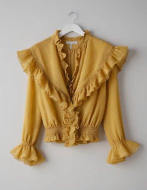 Elegant yellow frilled blouse displayed on a hanger against a neutral background. clipart