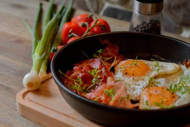 fried egg with bacon and vegetables on a wooden table in the kitchen.
