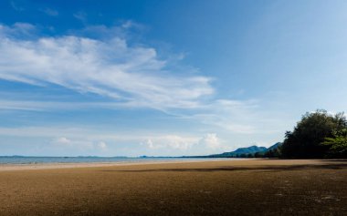 Sakin denizin üzerinde mavi gökyüzünü ve beyaz bulutları gösteren güzel tropik plaj manzarası, arka planda dağlar ve ağaçlar, Tayland 'da sakin ve huzurlu bir atmosfer yaratıyor, Chumphon