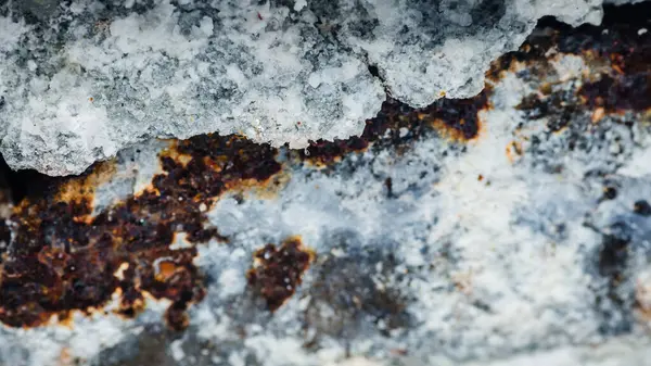 Paslı bir metal yüzeyi kaplayan tuz kristallerinin yakın çekimi, doğal paslanma etkilerini vurgulayan zıt dokular ve renklerden oluşan soyut bir desen oluşturur.
