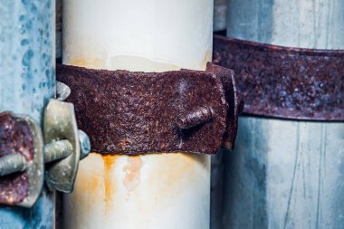 Paslı metal kıskaçlar paslanmış boruları sıkıca kavrıyor. Çürüme belirtileri gösteriyor. Yaşlanan endüstriyel altyapıda acil bakım ve onarım ihtiyacını vurguluyor.