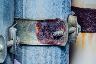 Galvanizli bir boruya tutunan paslanmış metal kıskaç, zamanla endüstriyel maddelerin üzerindeki paslanma ve yıpranma etkilerini gösteriyor, çürüme ve bozulma katmanlarını ortaya çıkarıyor.