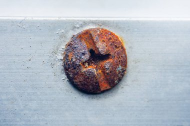 Metal bir yüzeye sabitlenmiş paslı bir vidanın yakın çekim görüntüsü zamanla aşınma ve bozulmanın çarpıcı etkilerini gösterir çürüme ve yaşlanma dokularını ortaya çıkarır.