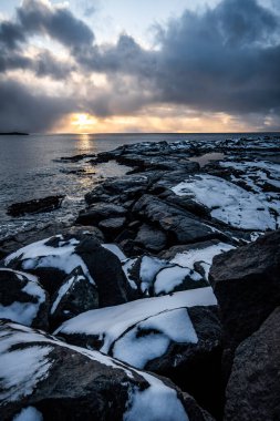 Akşamları karların altında kayalık bir sahille güzel bir deniz görüntüsü.