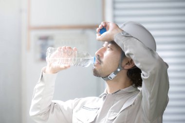 Genç Asyalı adam plastik şişeden su içiyor.