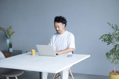 Kafede laptoplu ve kahve fincanlı Asyalı genç adam.