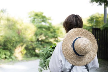 Yeşil bitkiler ve hasır şapkayla tarladaki kadın çiftçinin arka görüntüsü. 