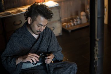 Kimono giymiş Asyalı bir gencin portresi ve geleneksel Japon evlerinde sake dolduruluyor.