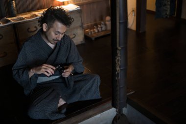 Kimono giymiş Asyalı bir gencin portresi ve geleneksel Japon evlerinde sake dolduruluyor.