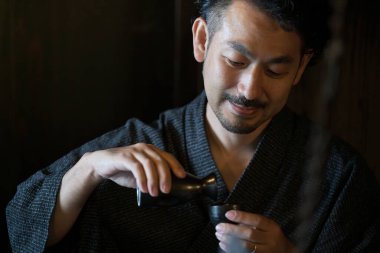 Kimono giymiş Asyalı bir gencin portresi ve geleneksel Japon evlerinde sake dolduruluyor.