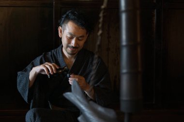 Kimono giymiş Asyalı bir gencin portresi ve geleneksel Japon evlerinde sake dolduruluyor.