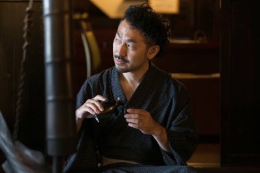 Kimono giymiş Asyalı bir gencin portresi ve geleneksel Japon evlerinde sake dolduruluyor.