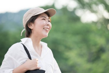 Açık havada çantasıyla gülümseyen Asyalı genç kadının portresi.