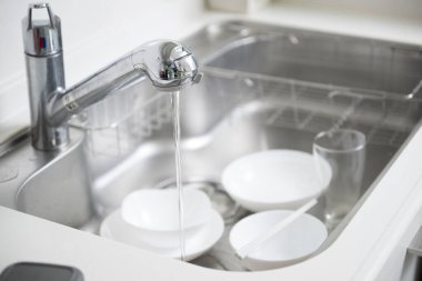 Mutfak lavabosundaki beyaz tabaklar, musluktan akan su.