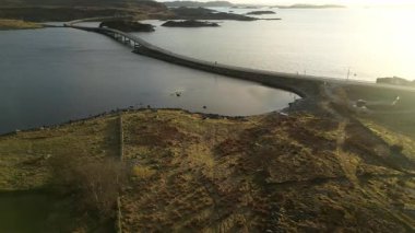 Norveç 'te, fiyordun yukarısında. Norveç 'te alışılmadık bir yapı, Norveç' teki fiyortlar arasında ilginç bir yol var. İnsansız hava aracı gün batımında bu sıra dışı yolda uçuyor. Güneş su yüzeyine yansıyor.