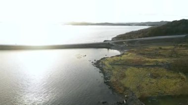 Norveç 'te okyanusun ortasında arabaların yarıştığı virajlı bir yolun ardından güneşli bir manzara.