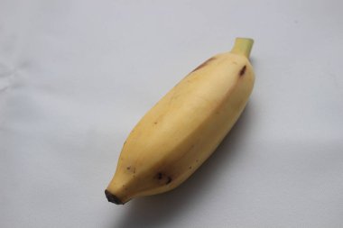 Beyaz desenli arka plana yerleştirilmiş tek bir olgun sarı muz. Meyve, hafif kahverengi benekli, doğal ışıklandırmayla fotoğraflanmış, yiyecek, beslenme veya tropikal meyvelerle ilgili kavramlar için idealdir..