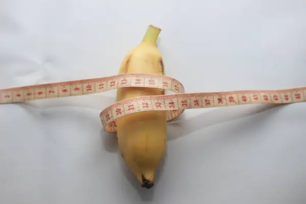 Ölçüm bandıyla sarılı kısa sarı bir muz, temiz beyaz bir arkaplan üzerine yerleştirilmiş. Bu resim, ölçüm, sağlık ve gıda porsiyonları ile ilgili kavramlara uygun olarak, meyvenin uzunluğunu ve çevresini vurgular..