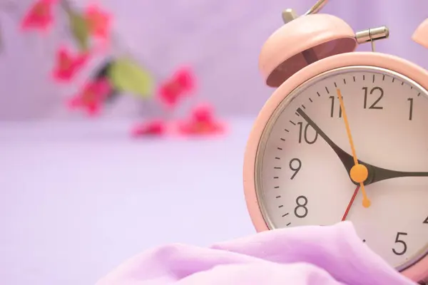 Pembe arka planda çalar saat ve çiçekler.