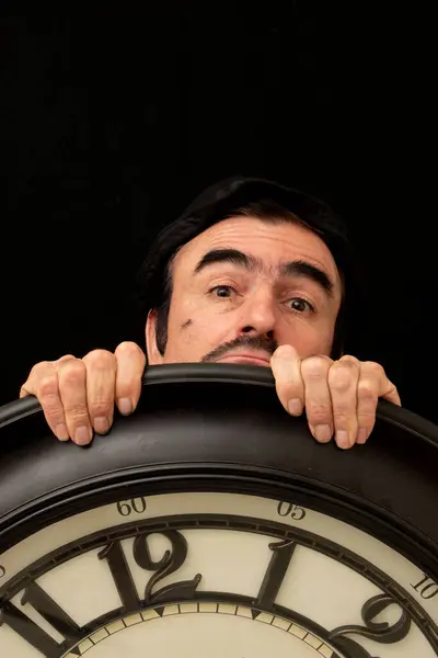 Siyah arka planda büyük bir saati olan bir adam.