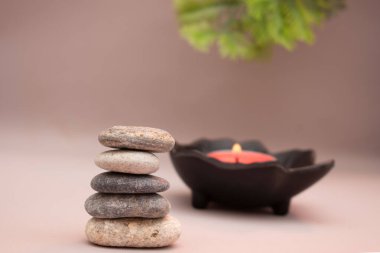 Yumuşak rulo havlular ve arka planda pastel çiçeklerle düzenlenmiş koyu renk spa taşları. Sıcak bej ayarı sakin ve huzurlu bir ortam yaratır. Sağlık, kaplıca ya da meditasyon için mükemmel..