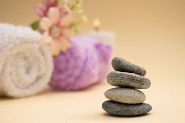 Yumuşak rulo havlular ve arka planda pastel çiçeklerle düzenlenmiş koyu renk spa taşları. Sıcak bej ayarı sakin ve huzurlu bir ortam yaratır. Sağlık, kaplıca ya da meditasyon için mükemmel..