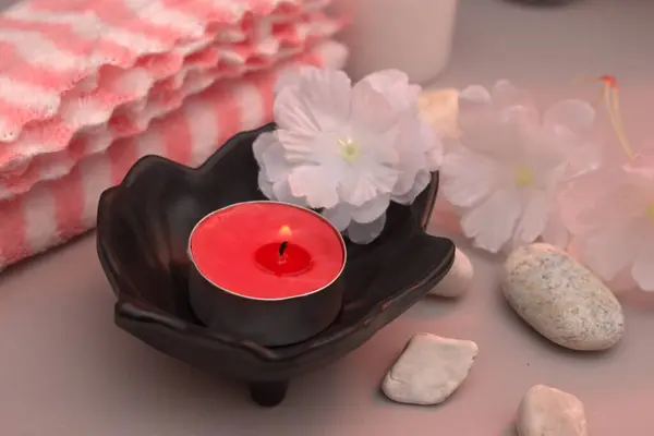 Yumuşak rulo havlular ve arka planda pastel çiçeklerle düzenlenmiş koyu renk spa taşları. Sıcak bej ayarı sakin ve huzurlu bir ortam yaratır. Sağlık, kaplıca ya da meditasyon için mükemmel..