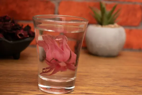 Tahta bir masanın üzerinde bir bardak pembe çiçek..