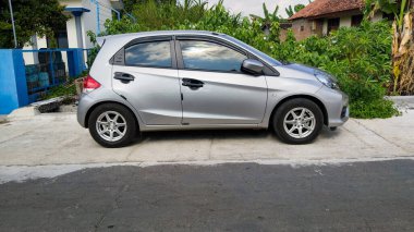 Endonezya 'da yeşillik ve evin yakınındaki iskan caddesinde park edilmiş gümüş renkli hatchback arabası, gündüz görüş açısı