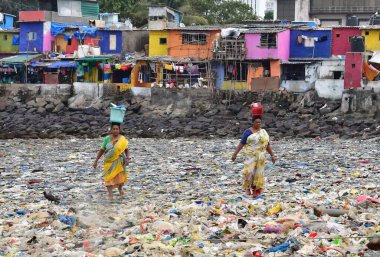 MUMBAI, INDIA - 27 Mayıs 2024 'te Hindistan' ın Mumbai kentinde, Badhwar Park yakınlarındaki Arap Denizi kıyısında toplanan çöpler arasında kadınlar yürür. (Fotoğraf: Bhushan Koyande / Hindustan Times)