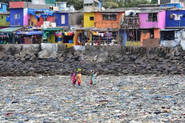 MUMBAI, INDIA - 27 Mayıs 2024 'te Hindistan' ın Mumbai kentinde, Badhwar Park yakınlarındaki Arap Denizi kıyısında toplanan çöpler arasında kadınlar yürüyor.. 