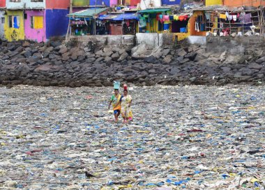 MUMBAI, INDIA - 27 Mayıs 2024 'te Hindistan' ın Mumbai kentinde, Badhwar Park yakınlarındaki Arap Denizi kıyısında toplanan çöpler arasında kadınlar yürüyor.. 