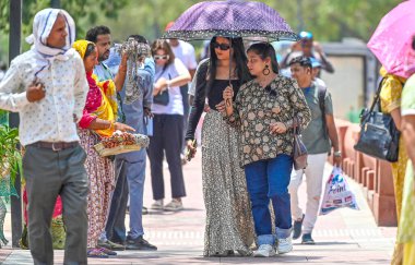 Hindistan Kapısı yakınlarındaki sıcak bir günde, 30 Mayıs 2024 'te Delhi-NCR sıcaklığı artarken, turistler kendilerini Atkı ve şemsiye altında koruyorlar.. 